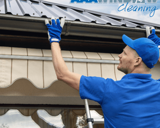 A man in blue cleaning gutters with gloves on
