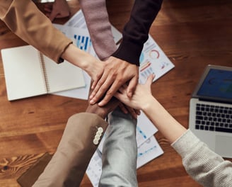 Diverse group of professionals joining hands in a teamwork gesture, symbolizing collaboration,