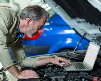 homem mexe em um laptop apoiado no motor do carro 