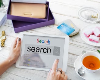 Tablet con la palabra search en pantalla, rodeada de objetos cotidianos como taza de té y cuaderno