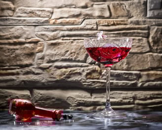 Cocktail rosso in coppa di cristallo con fiore di ciliegio su fondo in pietra – fotografia emozional