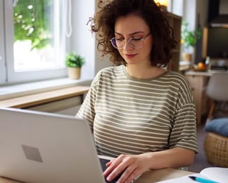 uma mulher de óculos, cabelos ondulados, mexendo em um notebook