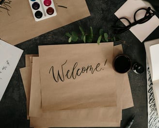 Handwritten welcome card surrounded by creative tools, symbolizing an open invitation...