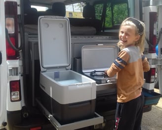 a young girl standing in front of a van with a coolerbox