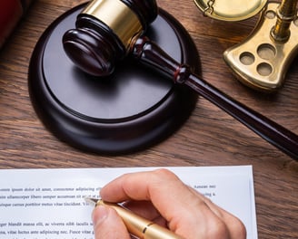 Judge's gavel sitting on a desk along with a hand holding a pen about to sign a document.