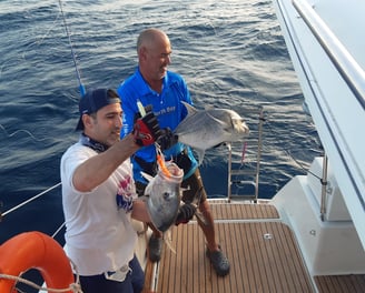 Anglers proudly showing their caught Giant Trevally on a catamaran - Catamaran Fishing Charters