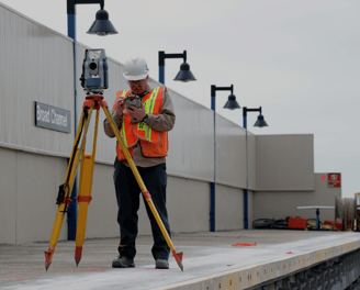 a man in a hard hat and safety vest using a tripod