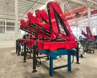Production line: Red SQZ68B.3 (3.2T) articulating knuckle boom cranes on blue stands, pre-vehicle mounting.