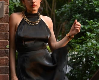 Cynthia Scellos in a black dress standing on a brick wall