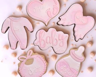 Baby shower themed cookies featuring baby essentials like a baby bottle, onesie, bib, and a cookie with the word baby