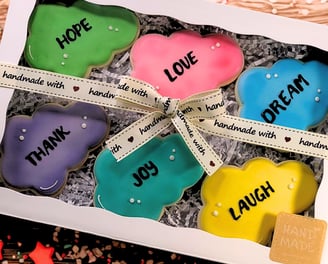 Set of cookies in a ready gift box decorated with royal icing, featuring positive words like Love, Dream, Laugh, Hope, Joy