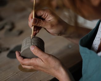 femme gravant des motifs à la main avec un outil en bois sur l'argile dans l'atelier de poterie