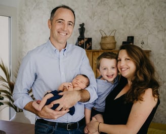 Photo de famille à domicile avec maman, papa, bébé et grand frère souriants – séance naissance Gard