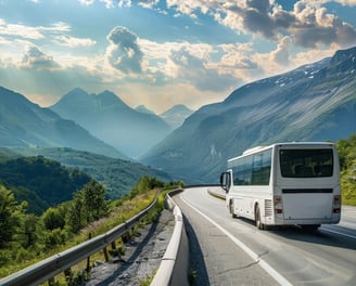 A white color bus travelling in a valley surrounded by mountains and greenery