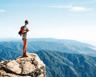 A women standing on a mountain rock and observing the beautiful view of a valley