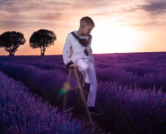 niño de comunion con traje de marinero sentado en escalera  en paisaje de flor de lavanda 