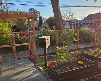 a hogwire garden fence and gate with landscaping planters