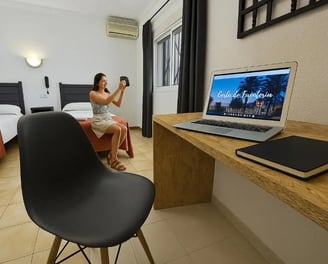 Habitación doble en Hotel San Vicente, con escritorio de madera, laptop y huésped tomando una foto.