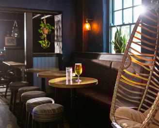 An egg chair next to some small round tables with drinks on 1 table