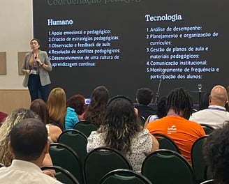 Jailana palestrando em um auditório, com um slide projetado que compara aspectos "Humano" e IA