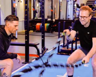 A man is exercising with battle ropes with a personal trainer