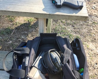 Black bag with ear protection and 2 self-defense firearms one with red dot one without.