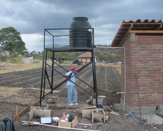 Jorge standing beneath a steel water tower used to feed the first two flush toilets in the community