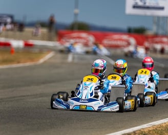 Plusieurs karts en course sur une piste, des pilotes portant des casques colorés et des karts marqués.