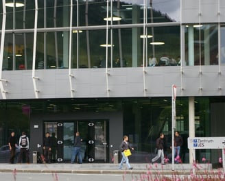 Auf dem Bild ist der Neubau der Montanuniversität Leoben zu sehen. Menschen benutzen den Gehweg.