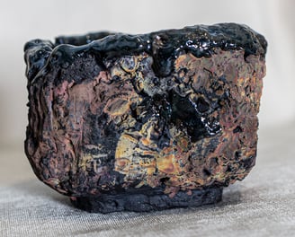 Raku-fired Kurinuki cup from Amman, Jordan, with black glaze, ochre tones, and volcanic textures