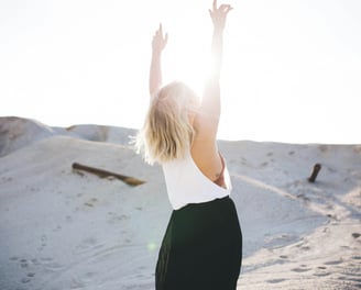 Une femme debout dans le sable, les bras levés, symbole de liberté et de bien-être