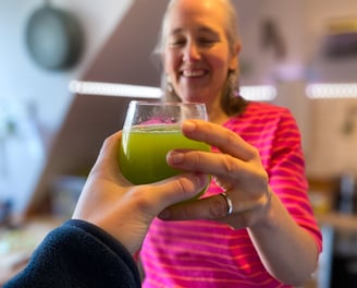 2 Hände reichen sich ein Glas Selleriesaft