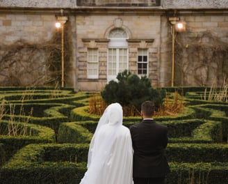 a bride and groom in formal attire standing in front of a castle