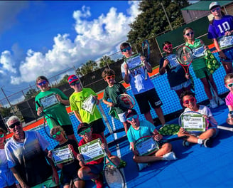 Kids holding rackets and summer camp certificates on tennis court.