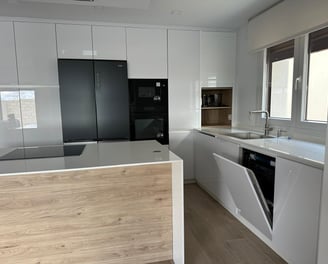 Cocina blanca y madera, isla central, electrodomésticos negros integrados.