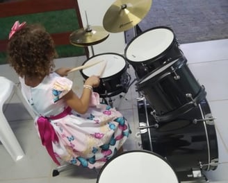 Criança sorridente tocando bateria em uma sala de aula de música, com foco e entusiasmo.