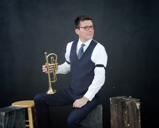 A man in a vest and tie is holding a cornet, looking to the side.