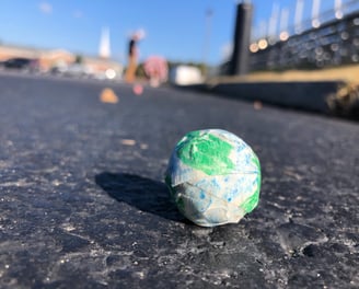 a small globe on the ground with students and school in the background