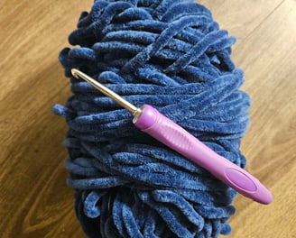 Une pelote de laine bleu avec un crochet violet