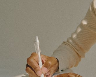 Mano di donna con pelle scura che scrive su un quaderno bianco con una penna trasparente