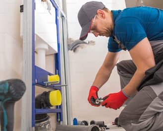 man hunched over, installing plumbing