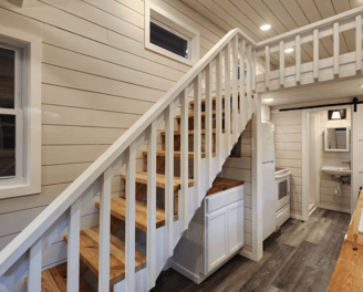 Wooden stairs and loft inside bright tiny home on wheels