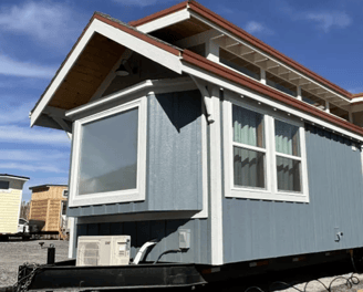 Blue and white tiny home on wheels with large windows