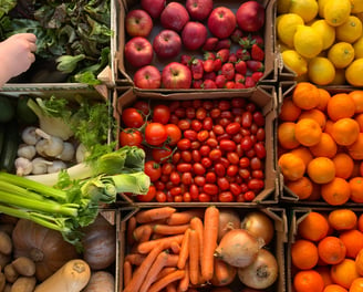 a person standing in front of a box of fruit and vegetables