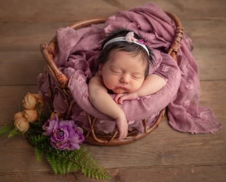 Una niña recién nacida durmiendo en una canasta con una flor en el cabello.