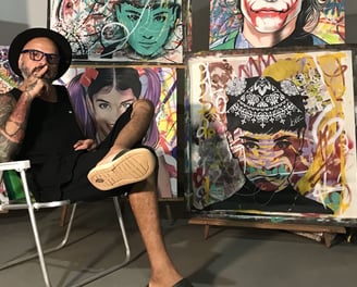 Sérgio Astral em seu estúdio, rodeado por suas obras de arte e materiais de pintura.