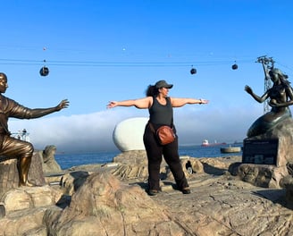 Trisha standing at Songdo Bay in Busan between the statue of the Mermaid and the villager