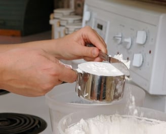 a person is holding a spoon and mixing a bowl of flour