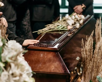 hand touching the dark brown stained coffin decorated by dried flowers