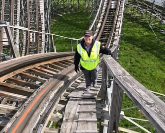 a woman in a safety vest is walking up a wooden roller coaster
